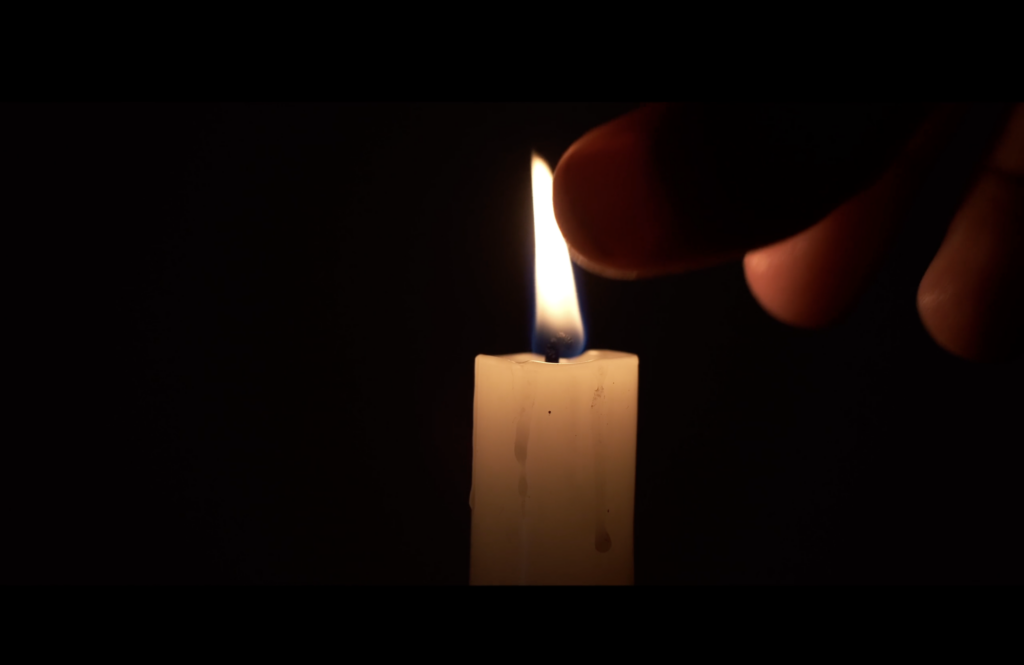 A photographic still from the short film Run Deep. The photo shows a candle that is about to be put out by someone pinching the wick.