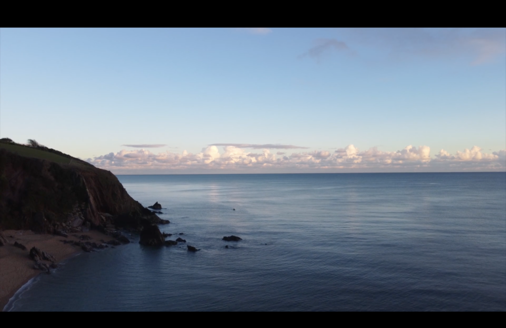 A photographic still from the short film The Artist. The photo shows a scene of a coastal cove with an extensive view of the ocean and clouds in the distance.